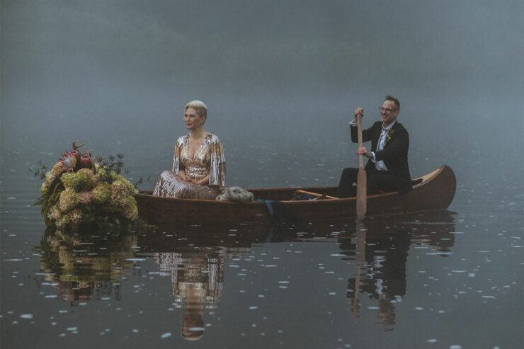 a just married couple rows a boat on a foggy lake