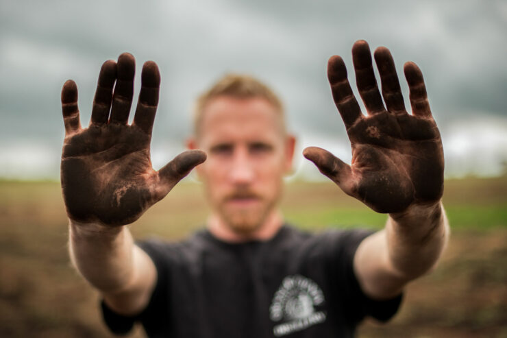man holding up hands covered in black dirt