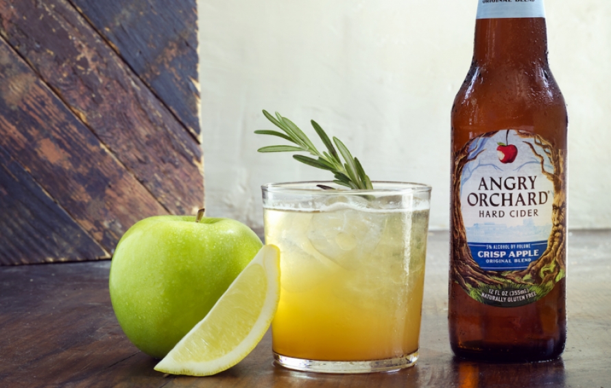 a cocktail, a green apple, a lemon wedge, and a bottle of angry orchard cider