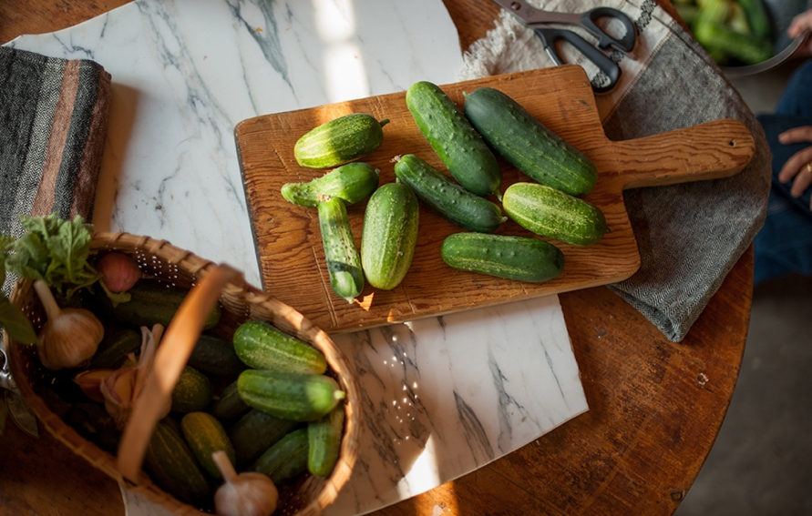 pickling cucumbers laid out on a cutting board and in a basket on a wooden table