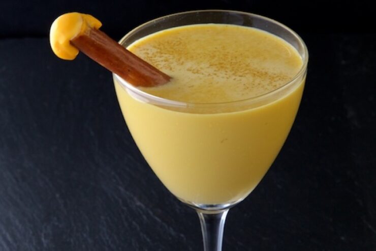 a yellow cocktail made with cheese with a pretzel garnish