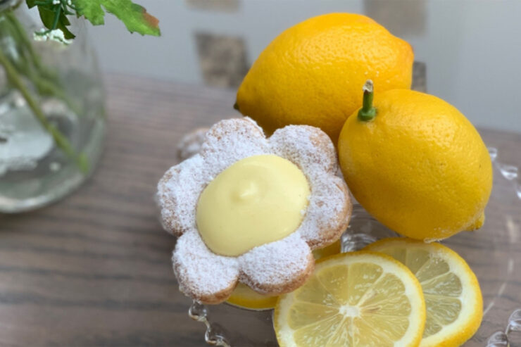 plate of lemons, lemon slices, and a daisy lemon tart on a wooden table next to a vase of daisies