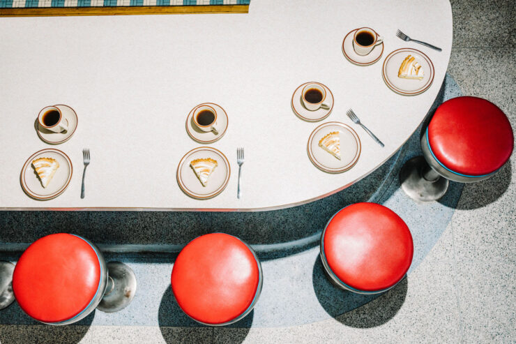 Retro dining table with four red seat bar stools and slices of pie and a cup of coffee in front of each stool