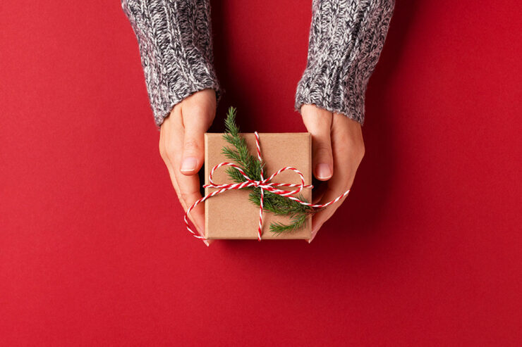 hands holding out gift wrapped in brown paper against red background